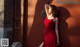 A woman in a red dress leaning against a wall.