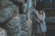 A naked woman standing in front of a stone wall.