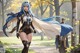 A woman with blue hair and a cape walking in a park.