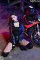 A woman in a leather jacket and fishnet stockings posing next to a motorcycle.