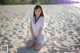 A woman sitting on a sandy beach next to the ocean.