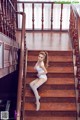 A woman in a white bodysuit sitting on a wooden staircase.