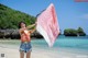 A woman standing on a beach holding a pink and white scarf.