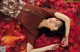 A woman laying on a bed of red leaves.